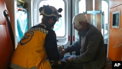 A Syrian White Helmet civil defense worker, left, treats an injured man inside an ambulance, in the town of Afrin, north of Aleppo, Jan. 20, 2022, in this photo provided by the Syrian Civil Defense White Helmets.