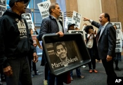 FILE - AIDS activists and others, some carrying an image of Turing Pharmaceuticals CEO Martin Shkreli in a makeshift cat litter pan, are asked to leave during a protest highlighting pharmaceutical drug pricing, in New York, Oct. 1, 2015.