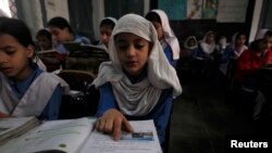 A girl reads a book while attending her daily class with others at a government school in Peshawar, Oct. 29, 2014. 