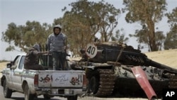 Rebel fighters armed with rocket propelled grenade launchers head back into Ajdabiya, past a previously destroyed pro-Gadhafi forces tank, during heavy shelling there, in Libya, April 10, 2011