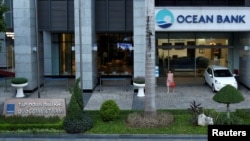 ແມ່ຍິງຜູ້ນຶ່ງກຳລັງຍ່າງອອກຈາກສາຂາທະນາຄານ Ocean Bank ຕັ້ງຢູ່ຕຶກ PetroVietnam ໃນນະຄອນຮາໂນ່ຍ ປະເທດຫວຽດນາມ. 