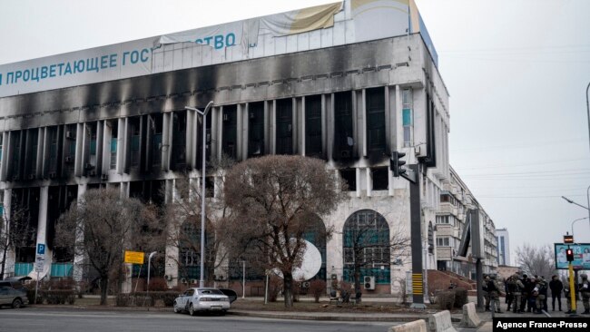 Binh sĩ Kazakhstan ngày 10/1 tuần tra và kiểm soát an ninh người đi bộ bên cạnh một tòa nhà chính phủ bị đốt cháy.