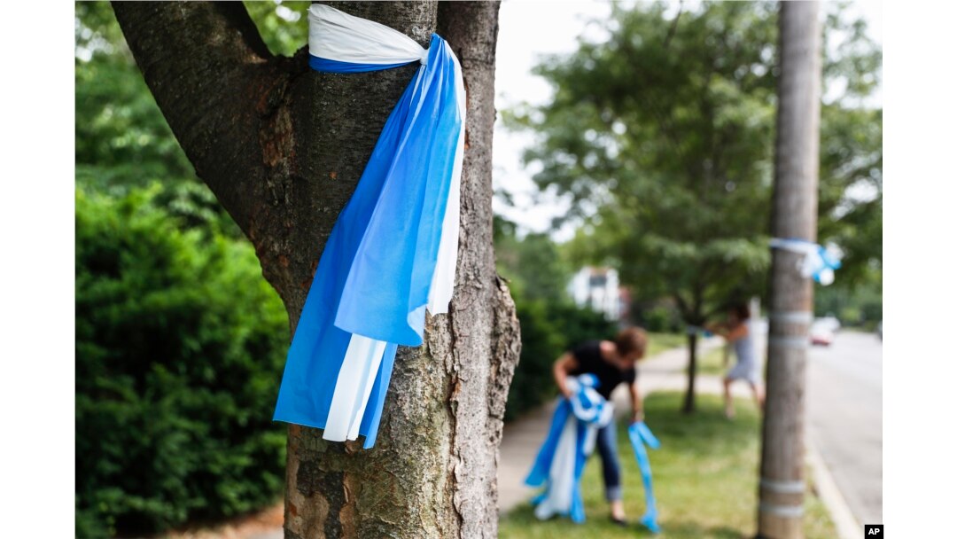 Alison Lebrun, center background, helps tie blue-and-white awareness ribbons near the family home of Otto Warmbier, in the Wyoming suburb of Cincinnati, Ohio, June 13, 2017.