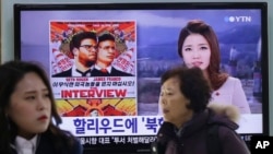 在韩国首尔的一个地铁站，人们走过一个正在播放新闻的电视屏幕，上面有索尼影业影片《采访》的海报。（资料图）
