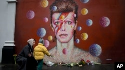 Una mujer y un niño colocan flores en un mural de David Bowie, el cantante británico que murió este lunes.