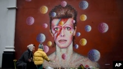 Warga setempat meletakkan bunga di dekat mural penyanyi David Bowie yang dilukis oleh Jimmy C di Brixton, London selatan (11/1). David Bowie meninggal dunia dalam usia 69 tahun akibat kanker.
