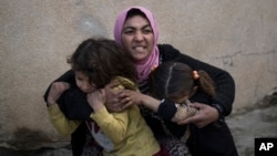 FILE - A woman holds her daughters as gunshots are heard in a neighborhood recently liberated by Iraqi security forces in western Mosul, Iraq, March 14, 2017. As the U.S.-led coalition ramps up the fight against the Islamic State group in Iraq and Syria, 