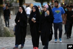 FILE - Iranian women make their way along a sidewalk while wearing chadors, a head-to-toe garment, in downtown Tehran, Iran, Aug. 24, 2017.
