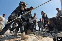 This photo provided by the Syrian Civil Defense White Helmets shows Civil Defense workers using machinery to search through the rubble after airstrikes hit in Khan Sheikhoun, in the northern province of Idlib, Syria, Sept, 24, 2017.