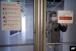 Kevin Gonzales, director of operations at the Rajen Kilachand Center for Integrated Life Sciences and Engineering, at Boston University, places safe distancing signage on glass doors on the school's campus, in Boston, Thursday, May 21, 2020. (AP Photo)