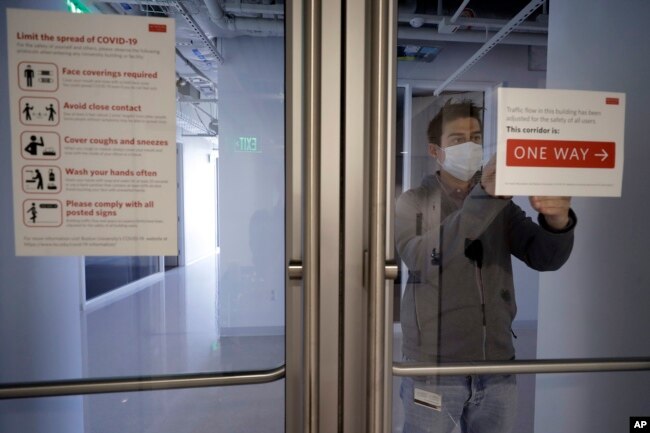 Kevin Gonzales, director of operations at the Rajen Kilachand Center for Integrated Life Sciences and Engineering, at Boston University, places safe distancing signage on glass doors on the school's campus, in Boston, Thursday, May 21, 2020. (AP Photo)