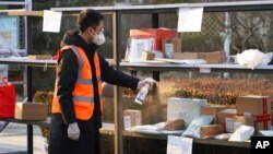 FILE - In this photo released by Xinhua News Agency, a staff member disinfects parcels at a community where a locally transmitted COVID-19 case was found, in Haidian district, Beijing, China, Jan. 18, 2022.