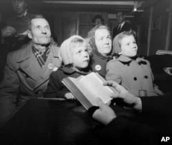 Kusma Kandaurow, 61, and his wife, Sofie, 41, and their children, Hanna, left, front, 9, and Sonja, 5, are in deep thought as a clergyman reads scripture following their arrival in New York City, Dec. 16, 1955, with other refugees aboard the Navy transport General Langfitt. They were brought to the United States under the Refugee Relief Act of 1953, in the program of the Episcopal Church in the U.S. and the Church World Service's Resettlement Program.