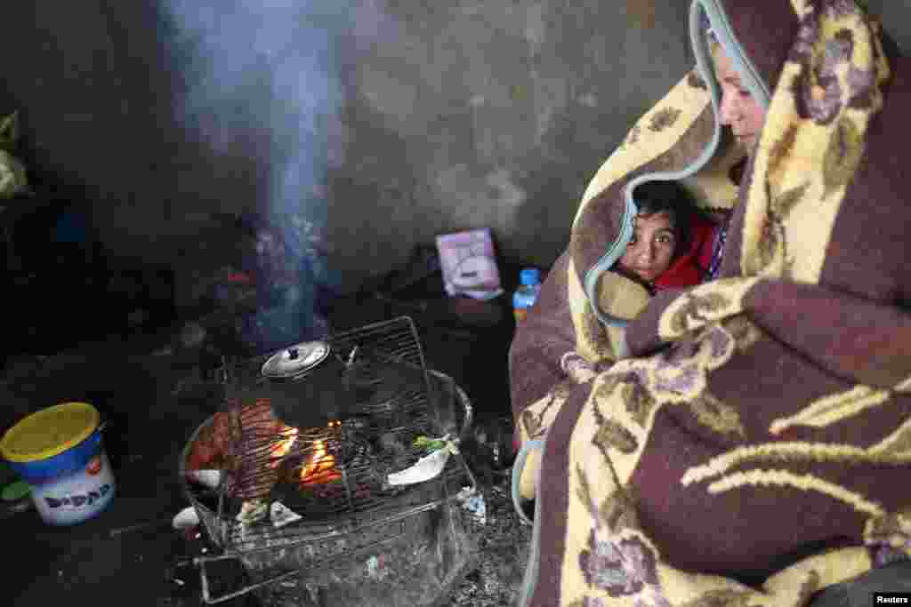 A Palestinian woman and her daughter, wrapped with a blanket, sit by a fire as they make tea inside their dwelling during a winter storm in Khan Younis in the southern Gaza Strip.