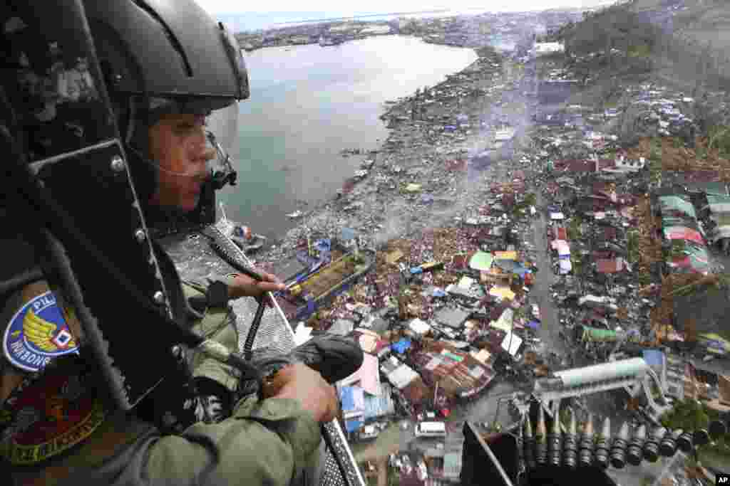 A Philippine Air Force crew looks out from his helicopter as Typhoon Haiyan-ravaged city of Tacloban is seen in the background, during a flight to deliver relief goods, Nov. 19, 2013.
