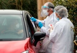 Medical staff test a person in their car with COVID-19 symptoms, at a drive-through testing site outside a medical biology laboratory in Anglet, southwestern France, Monday, April 20, 2020. (AP Photo/Bob Edme)