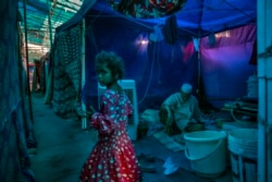 A young Rohingya refugee girl walks past an elderly man sitting inside a tent at a refugee camp alongside the banks of the Yamuna River in the south-eastern borders of New Delhi. (AP Photo/Altaf Qadri)