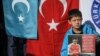 Seorang pendukung minoritas Muslim Uighur di China menunjukkan poster Mesut Ozil, pemain Arsenal asal Jerman yang berdarah Turki melintasi bendera Turkestan Timur dan Turki di Lapangan Beyazid, Istanbul, 14 Desember 2019. (Foto: AFP)