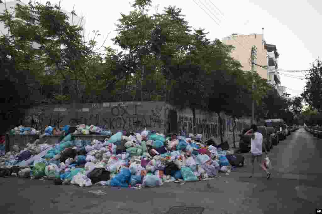 A woman walks past a pile of trash — and a message on the wall in Greek that reads "No garbage" — in the Kaminia neighborhood of Piraeus, near Athens. Greece's municipal garbage collectors are on a 14-day protest strike that has left mounds of festering refuse piled up across Athens amid high summer temperatures.