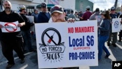 Alec Young, a shipfitter at Bath Iron Works, center, demonstrates against COVID-19 vaccine mandates outside the shipyard, Oct. 22, 2021, in Bath, Maine.