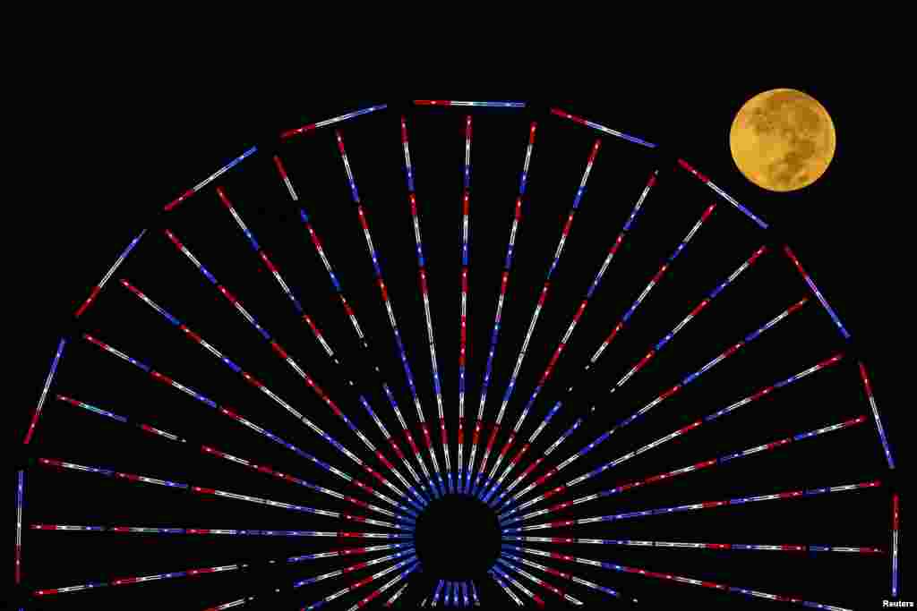 The moon is pictured behind a ferris wheel on the pier in Santa Monica, California after a total lunar eclipse, also known as a "blood moon", Oct. 8, 2014.