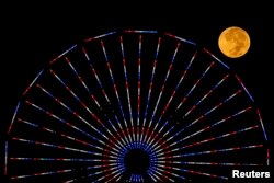 FILE - The moon is pictured behind a Ferris wheel on the pier in Santa Monica, California after a total lunar eclipse, also known as a "blood moon," Oct. 8, 2014.
