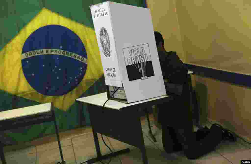 A man kneels down in a voting booth as he casts his vote during Brazil's general elections at a polling station in Sao Bernardo do Campo, near Sao Paulo, Oct. 5, 2014. 