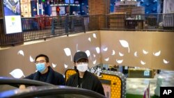 Una pareja usa máscaras faciales mientras suben por una escalera mecánica en un centro comercial en Beijing, el sábado 7 de marzo de 2020.