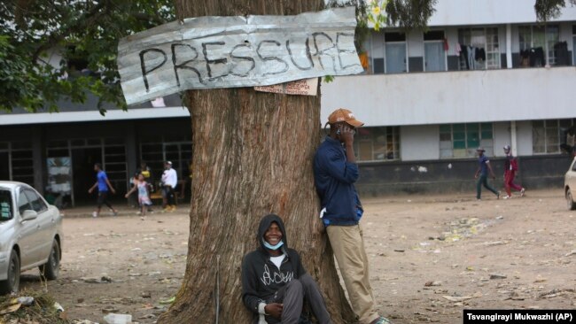 Two men take a break under a tree in a poor community outside the capital Harare on November 16, 2021. (AP Photo/Tsvangirayi Mukwazhi)