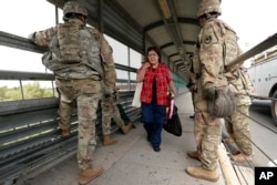 Pedestrians pass members of the U.S.military working to place razor wire along the U.S.-Mexico border on the McAllen-Hidalgo International Bridge, Nov. 2, 2018, in McAllen, Texas.