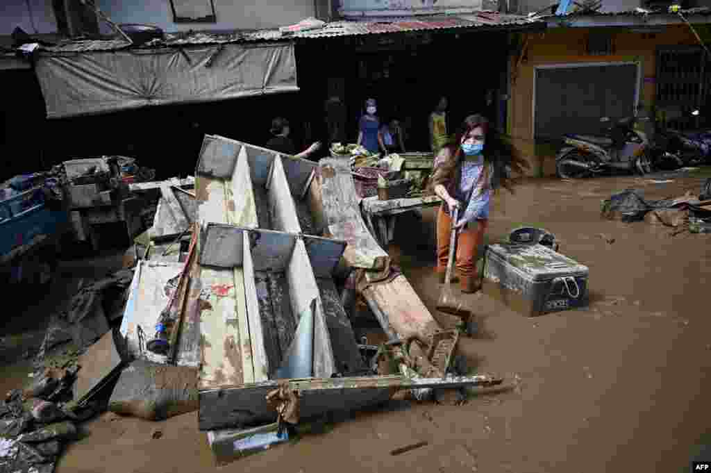 A resident uses a dust pan to shovel away muddy water next to debris in front of her flood-damaged home a day after Typhoon Vamco hit, in a residential area in Marikina City, suburban Manila.