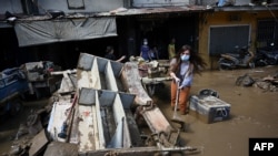 Seorang perempuan sedang berusaha membersihkan umpur di samping puing-puing di depan rumahnya yang rusak akibat banjir sehari setelah Topan Vamco melanda, di daerah pemukiman di Kota Marikina, pinggiran kota Manila. (Foto: AFP)