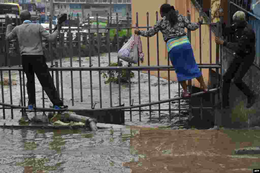 Pedestrian use a metal fence to cross the flooded road on their way to work following heavy rainfal in Nairobi, Kenya.