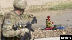 An Afghan girl washing clothes in a river looks at a US Army soldier in the town of Senjaray, southern Afghanistan May 29, 2012.