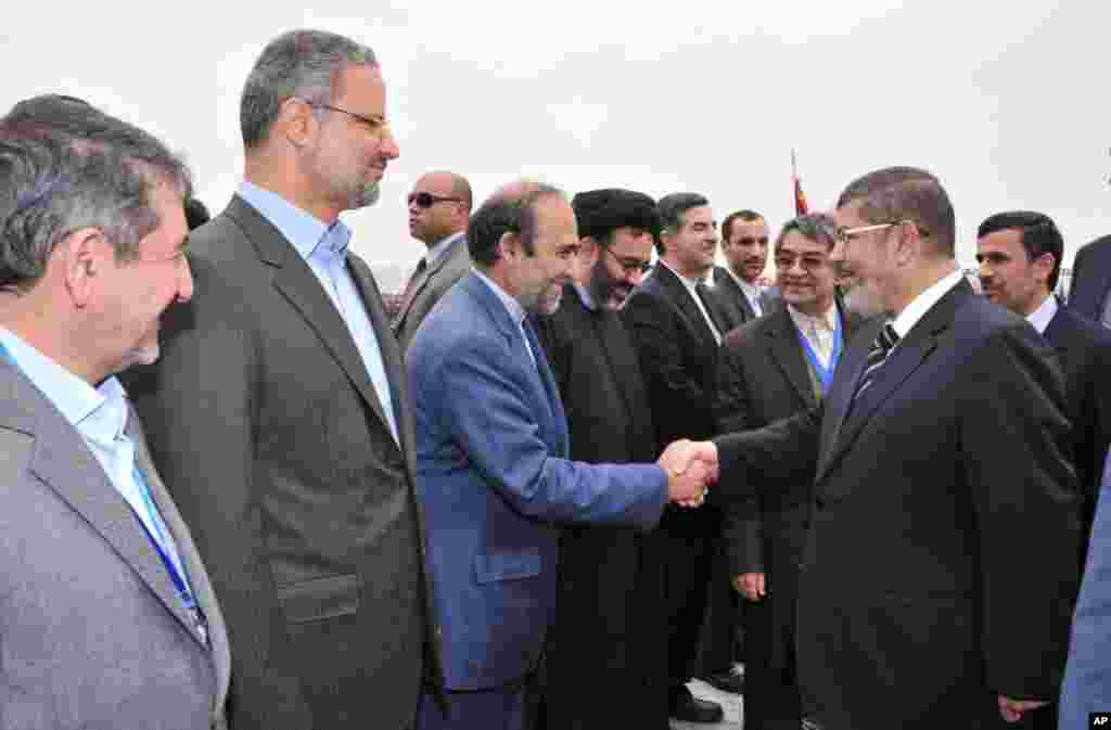 Iran's President Mahmoud Ahmadinejad looks on as Egyptian President Mohamed Morsi shakes hands with the Iranian delegation at the airport in Cairo, Egypt, February 5, 2013. (Egyptian Presidency Handout)