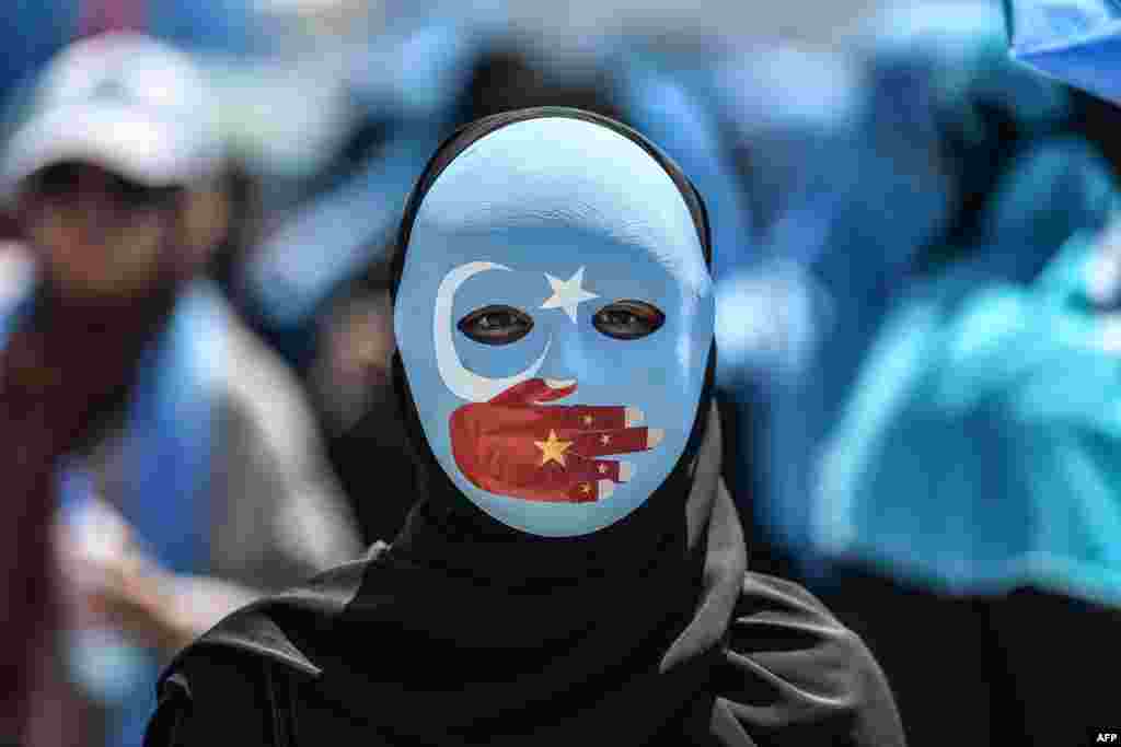 A demonstrator wearing a mask painted with the colors of the flag of East Turkestan and a hand bearing the colors of the Chinese flag attends a protest against China's treatment of ethnic Uighur Muslims during a deadly riot in July 2009 in Urumqi, in front of the Chinese consulate in Istanbul, Turkey. 