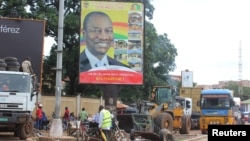 FILE - People pass in front of an electoral campaign poster for incumbent President Alpha Conde in Conakry, Guinea, Sept. 10, 2015. 