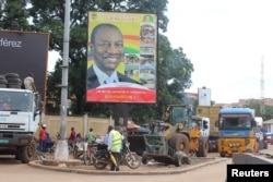 People pass in front of an electoral campaign poster for incumbent President Alpha Conde in Conakry, Guinea, Sept. 10, 2015.