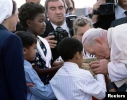 Pope John Paul II kisses a basket of South African soil presented to him by four children of different races as he arrives at Johannesburg International Airport, Sept. 16, 1995, at the start of his first official visit to the country.