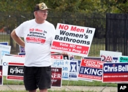 FILE - A man holds a sign that reads, "No men in women's bathrooms" while protesting in Houston, Oct. 21, 2015.