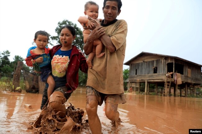 Parents carry their children as they leave their home during the flood after the Xe Pian Xe Namnoy hydropower dam collapsed in Attapeu province, Laos, July 26, 2018.