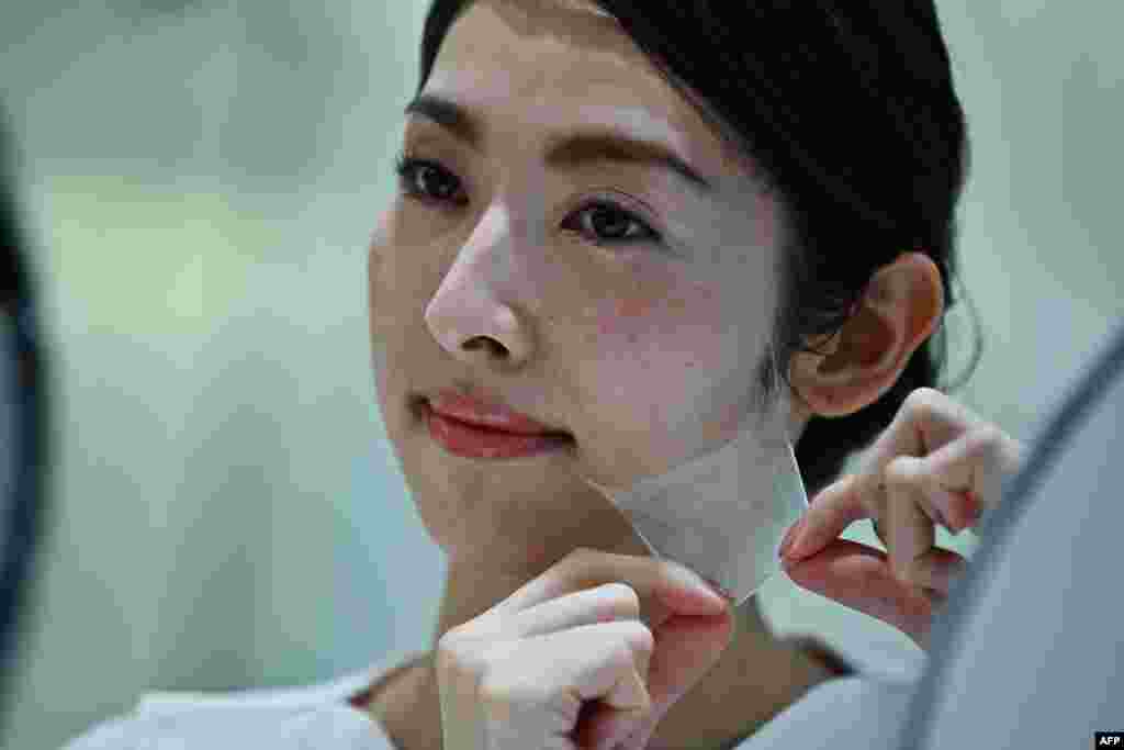 An employee for Japanese makeup company Kao removes a thin transparent layer after using a diffuser on her face, during a product demonstration in Tokyo, December 4, 2019. The company presented to the public what it said was the world&#39;s first spray-on skin, using fibers 1/100th the thickness of a human hair to form a covering for the face.