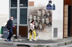 Pejalan kaki berjalan melewati karya seni seniman jalanan Perancis Christian Guemy, yang juga dikenal sebagai C215, untuk menghormati anggota majalah satire Charlie Hebdo,