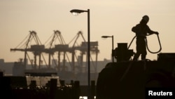 A worker holds a rope in front of cranes during sunset at a port in Tokyo, Japan, Dec. 9, 2015. A trade union survey has found that its members work an average of 40 hours of overtime a month, but are paid for only 22.7.