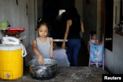 FILE - One of Yennifer Padron and Victor Cordova's daughters touches hot water in a pot in the house where they live at Petare slum in Caracas, Venezuela, Aug. 21, 2017.