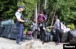 A family who identified themselves as from Haiti are confronted by a Royal Canadian Mounted Police officer as they try to enter into Canada from Roxham Road in Champlain, New York, Aug. 7, 2017.