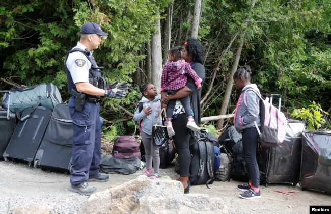 A family who identified themselves as from Haiti are confronted by a Royal Canadian Mounted Police officer as they try to enter into Canada from Roxham Road in Champlain, New York, Aug. 7, 2017.