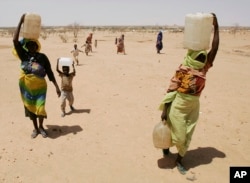 FILE - Women carry water across the Iridimi refugee camp near Iriba in eastern Chad, Sept. 25, 2004.