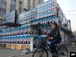 FILE - A woman cycles past a building covered in portraits of Chinese President Xi Jinping in Shanghai, March 26, 2016.