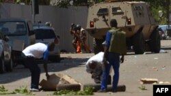 Transeúnes observan mientras personal de seguridad desciende de un vehículo blindado en Uagadugú, la capital de Burkina Faso, el viernes, 2 de marzo de 2018.